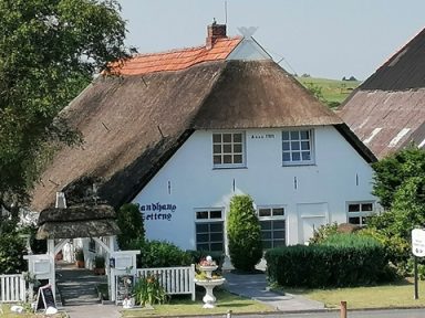 Traditionelles, weißes Haus mit Reetdach und grünem Garten.