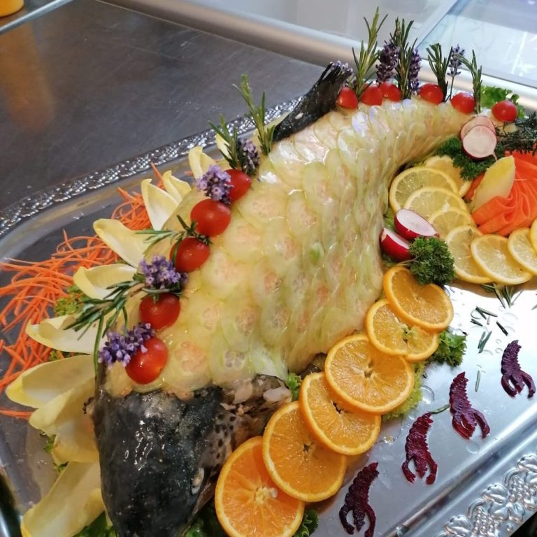 Ein kunstvoll angerichteter Fisch mit Obst und Gemüse auf einem silbernen Tablett.