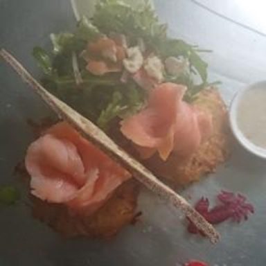 Kartoffelpuffer mit Räucherlachs, Salat und einer kleinen Schale Sauce.