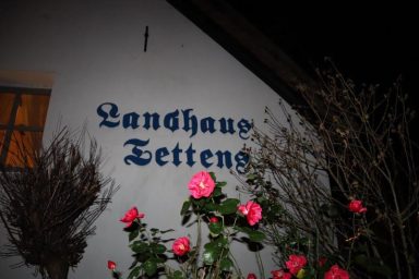 Hauswand mit der Aufschrift "Langhaus Tettens" und blühenden Pflanzen im Vordergrund.