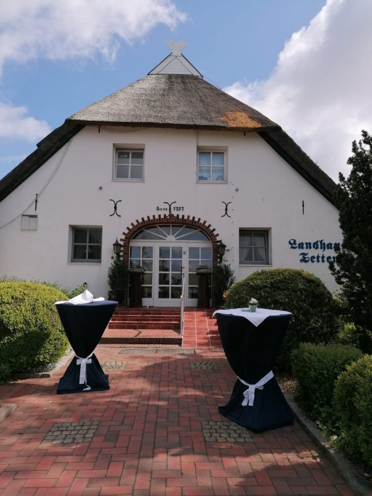 Helles Gebäude mit spitzem Dach, Eingangsbereich und dekorierten Stehtischen.