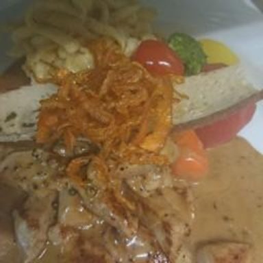 Gegrilltes Fleisch mit Sauce, Gemüsegarnitur und knusprigen Zwiebeln auf einem Teller.